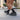 A runner crouches on a city sidewalk, adjusting their black socks. They're wearing black, thick-soled running shoes. Cars and buildings blur in the background.