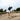 A golfer wearing a dark top and white skirt skillfully hits a sand shot. The scene is set in a lush golf course under an overcast sky, conveying focus.